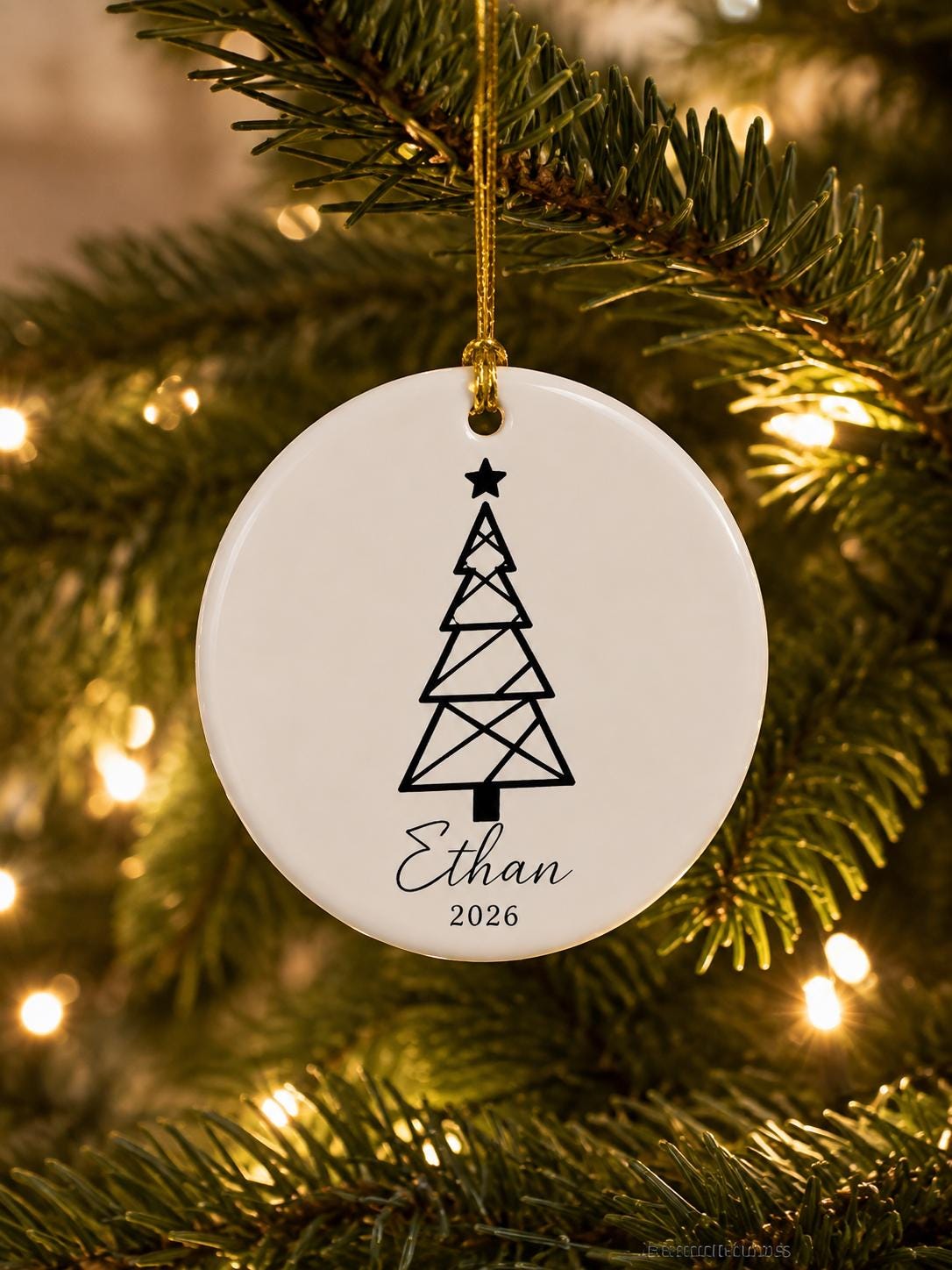 Round ceramic ornament with a geometric line-art Christmas tree and the name Ethan 2026 hanging on a tree