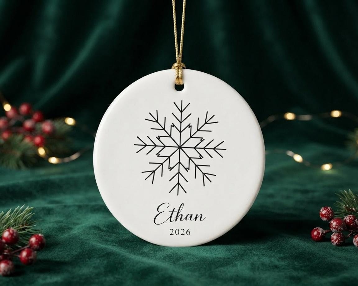 Round ceramic ornament with a line-art snowflake and the name Ethan 2026 on a gold string