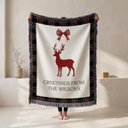 Person holding up the reindeer family name Christmas blanket with a dark tartan border and fringe