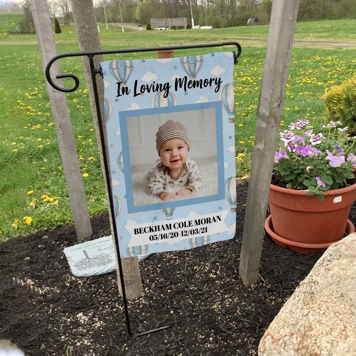 Baby In Loving Memory hot air balloon photo memorial garden flag on a garden flag stand in a yard with potted flowers