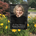 Black In Loving Memory portrait garden flag with name and dates in a garden bed with yellow lilies