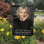 Black In Loving Memory portrait garden flag with name and dates in a garden bed with yellow lilies