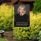 Black In Loving Memory portrait garden flag with name and dates in front of bright yellow shrubs