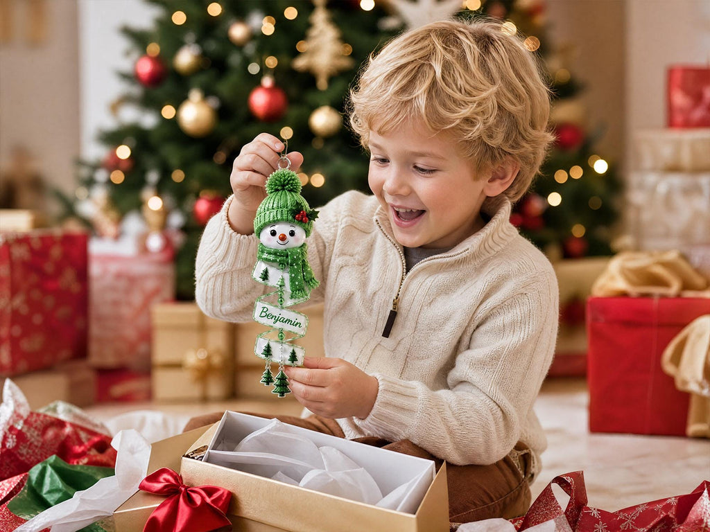 Boy unboxing a green snowman ornament with the name Benjamin in front of a Christmas tree
