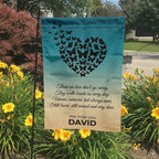 Butterfly heart Those We Love Don't Go Away memorial garden flag in a garden bed with yellow lilies