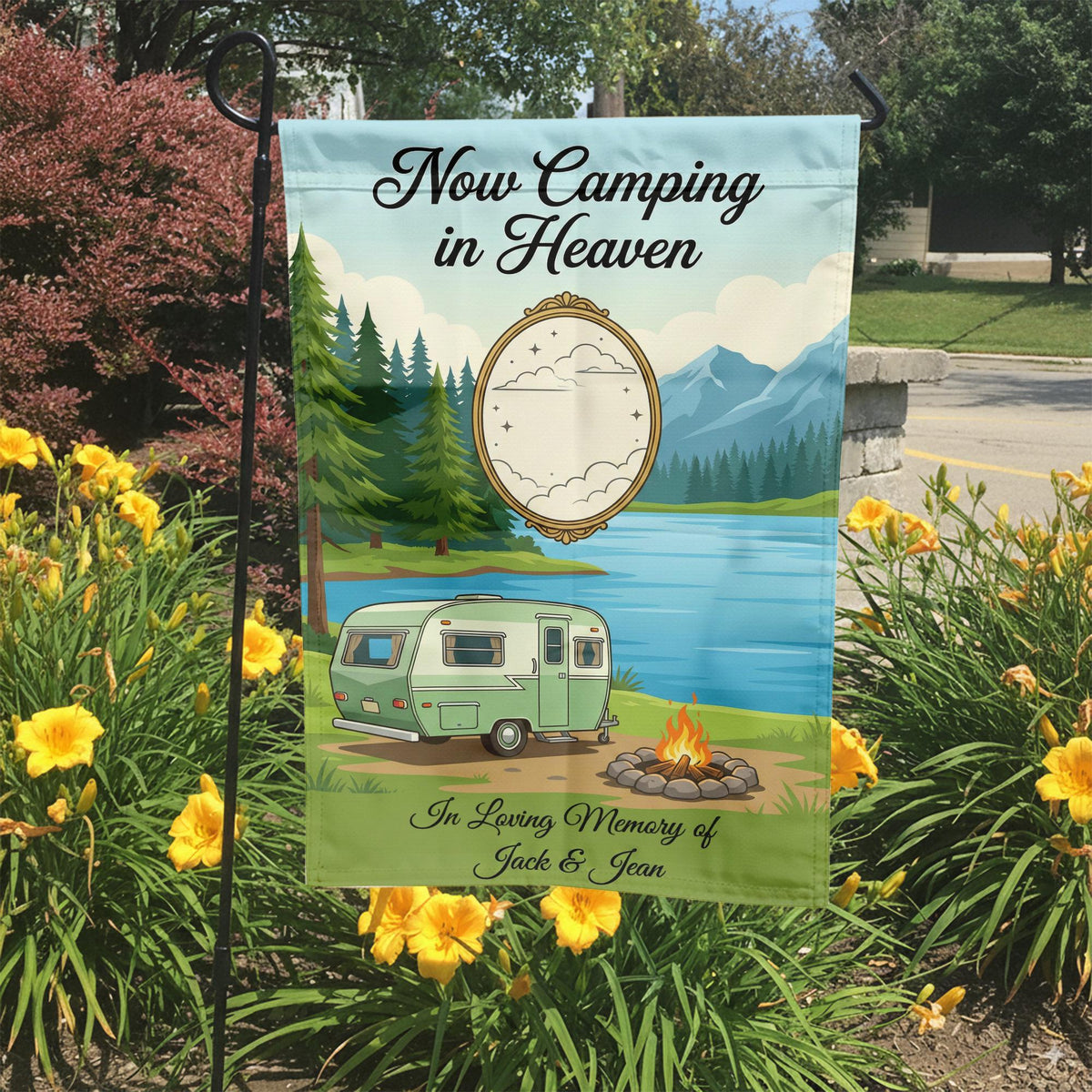 Now Camping in Heaven memorial garden flag with a vintage camper by a mountain lake in a garden bed with yellow lilies