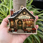 Hand holding a personalized Christmas flower shop wooden ornament outdoors among plants