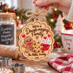 Hand holding a baking family Christmas ornament above a counter with cookie cutters