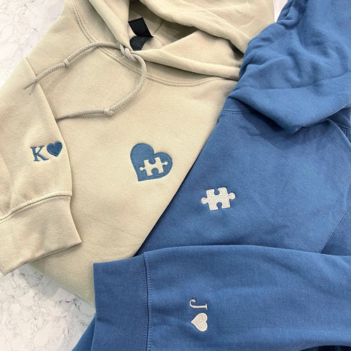Embroidered puzzle heart on a sand hoodie with the initial K and a heart on the sleeve