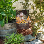 Fall memorial photo garden flag with sunflowers, poem and name in a flower bed beside a wooden barrel planter