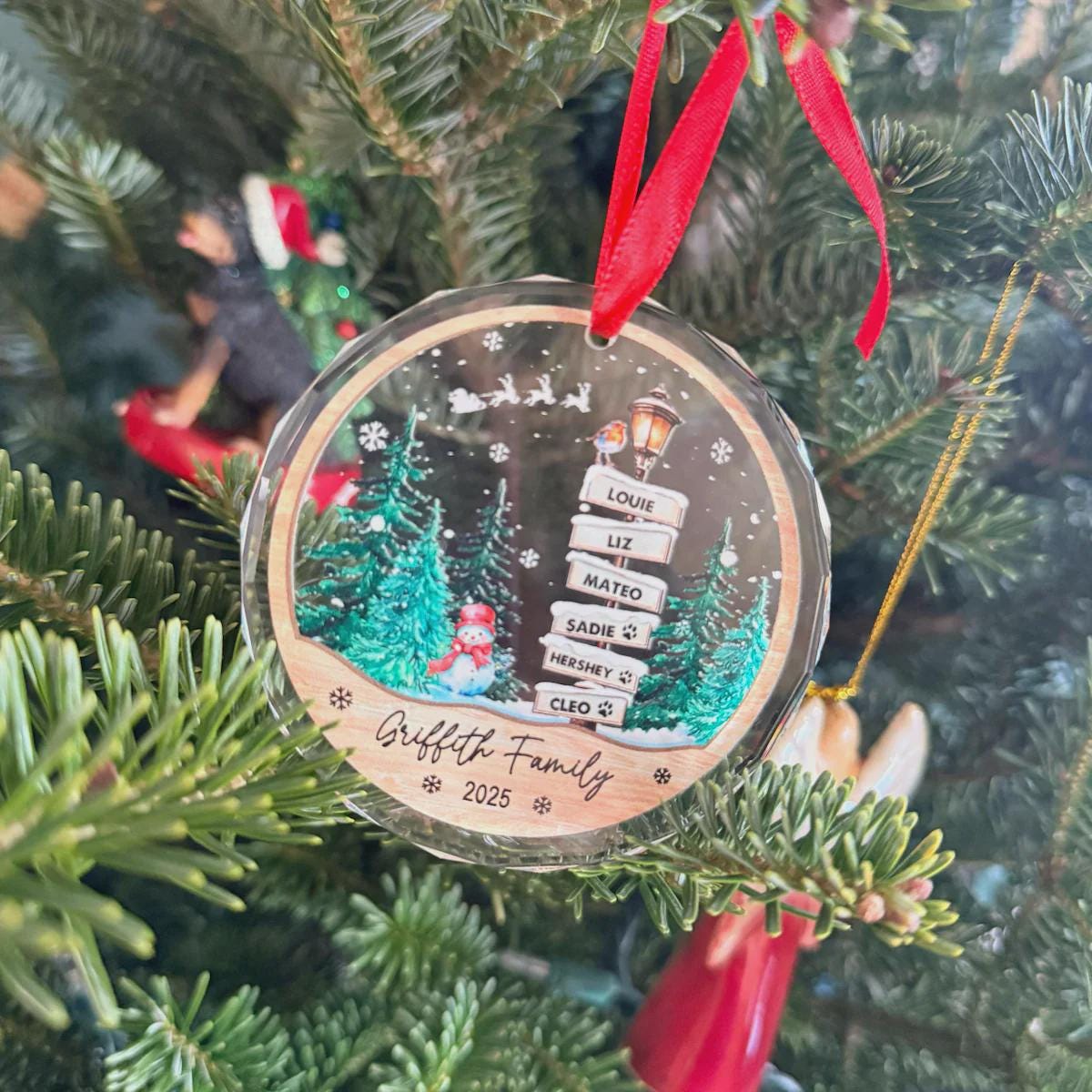 Family signpost acrylic ornament with a red ribbon hanging on a Christmas tree