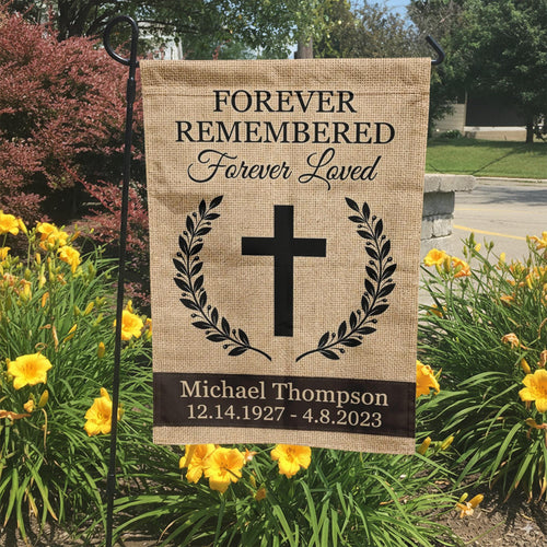 Forever Remembered Forever Loved cross memorial garden flag with burlap look in a garden bed with yellow lilies