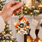 Hand hanging a fox with lantern Christmas wooden ornament with name Olivia by a fireplace