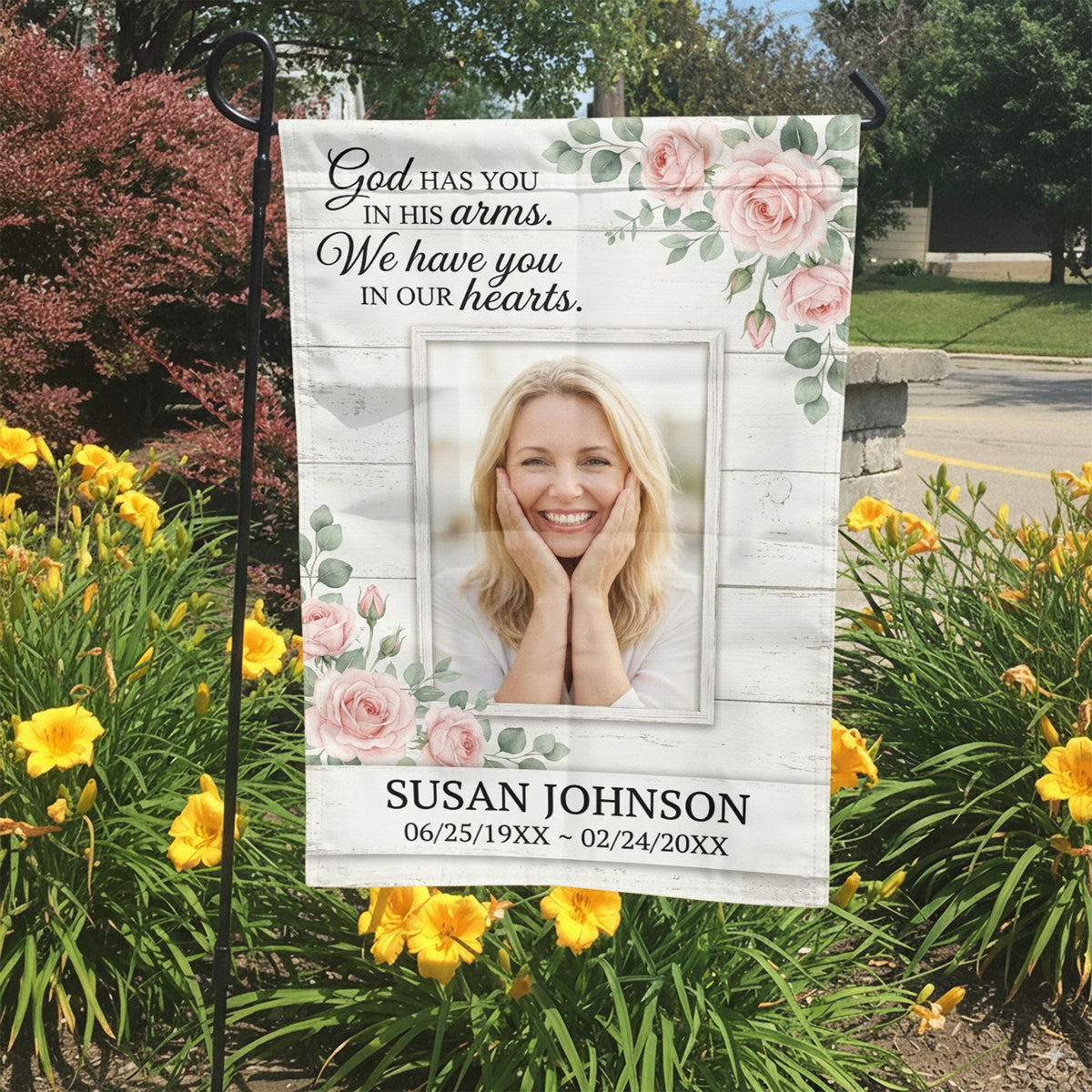God Has You In His Arms pink rose photo memorial garden flag in a garden bed with yellow lilies