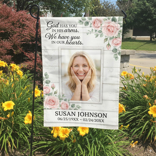 God Has You In His Arms pink rose photo memorial garden flag in a garden bed with yellow lilies