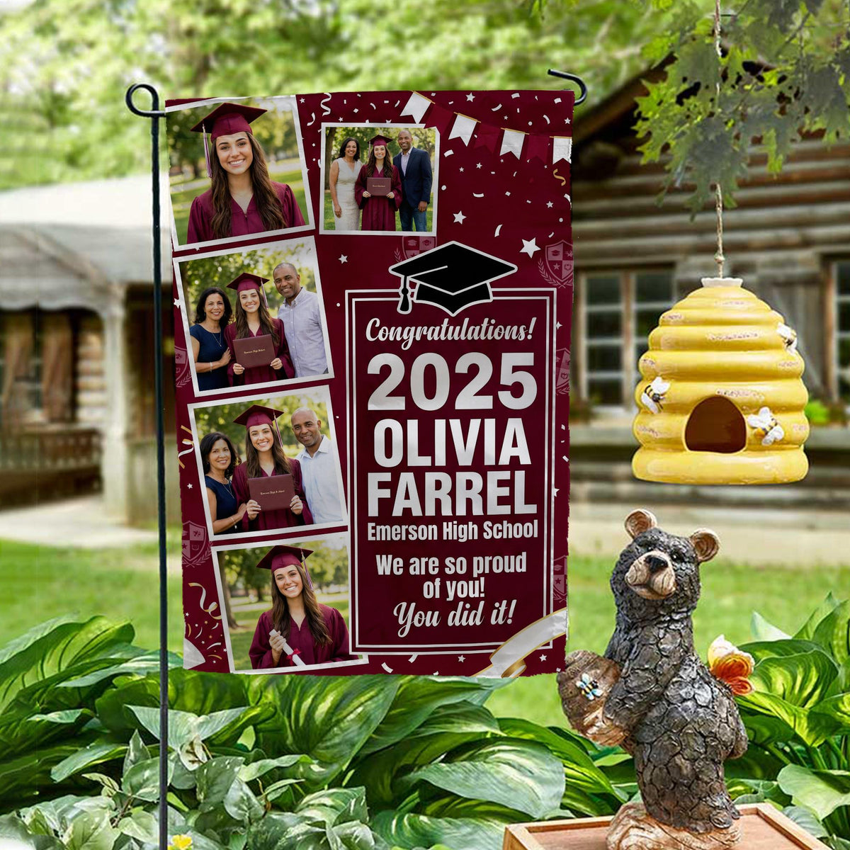 Maroon graduation photo collage garden flag with grad year, name and school on a garden stand by a log cabin with a beehive and bear statue
