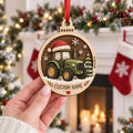 Hand holding a personalized round green tractor wooden ornament with Santa hat and name