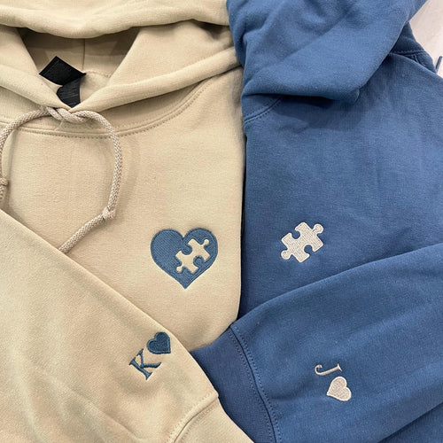 Sand and blue couple hoodies with an embroidered heart and puzzle piece and initials K and J on the sleeves