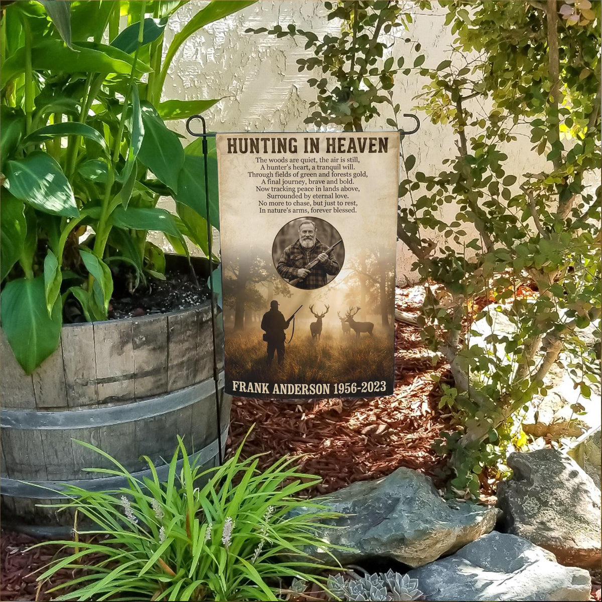 Hunting In Heaven photo memorial garden flag with a hunter and deer at sunrise in a flower bed beside a wooden barrel planter