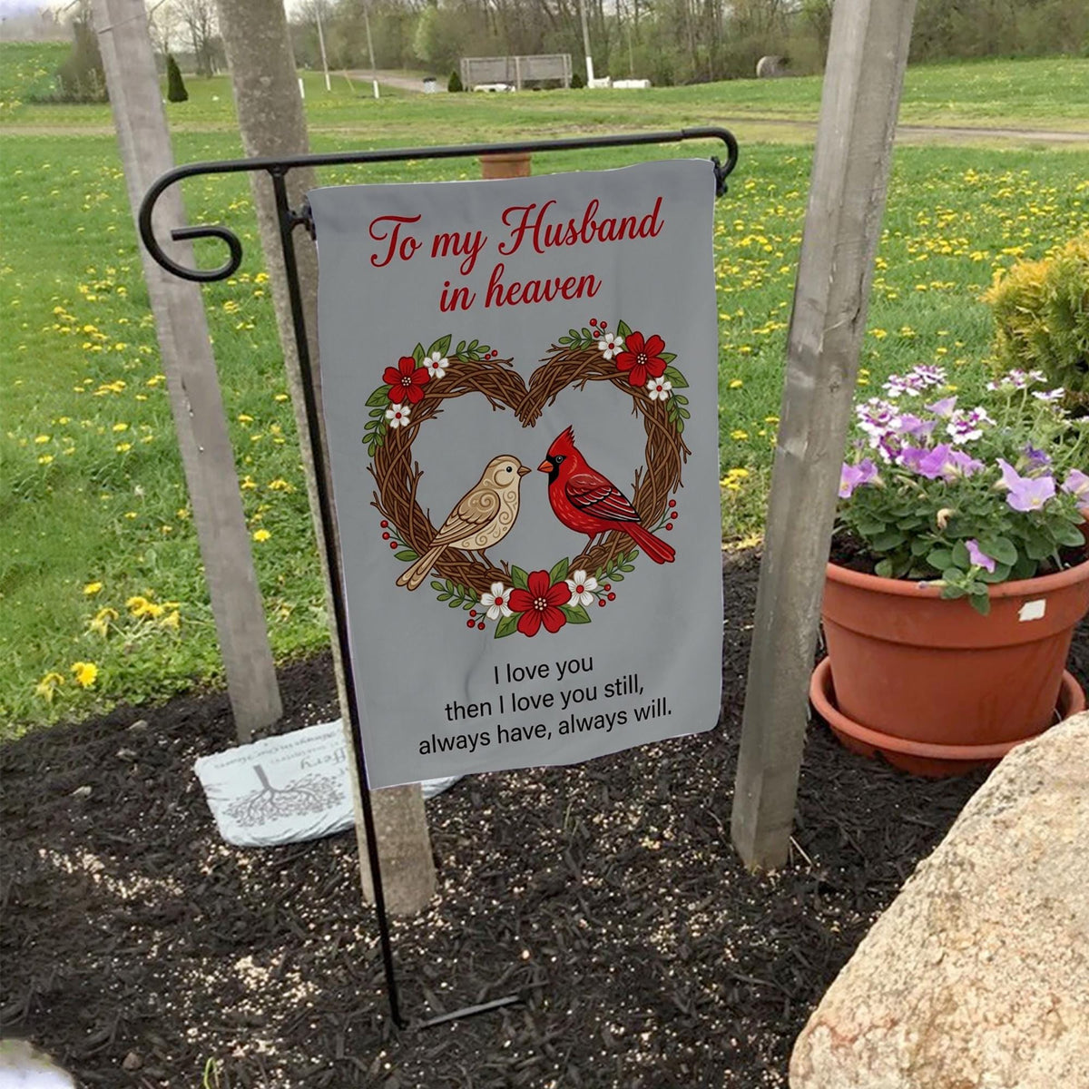 To My Husband In Heaven cardinal heart wreath memorial garden flag on a garden flag stand in a yard with potted flowers