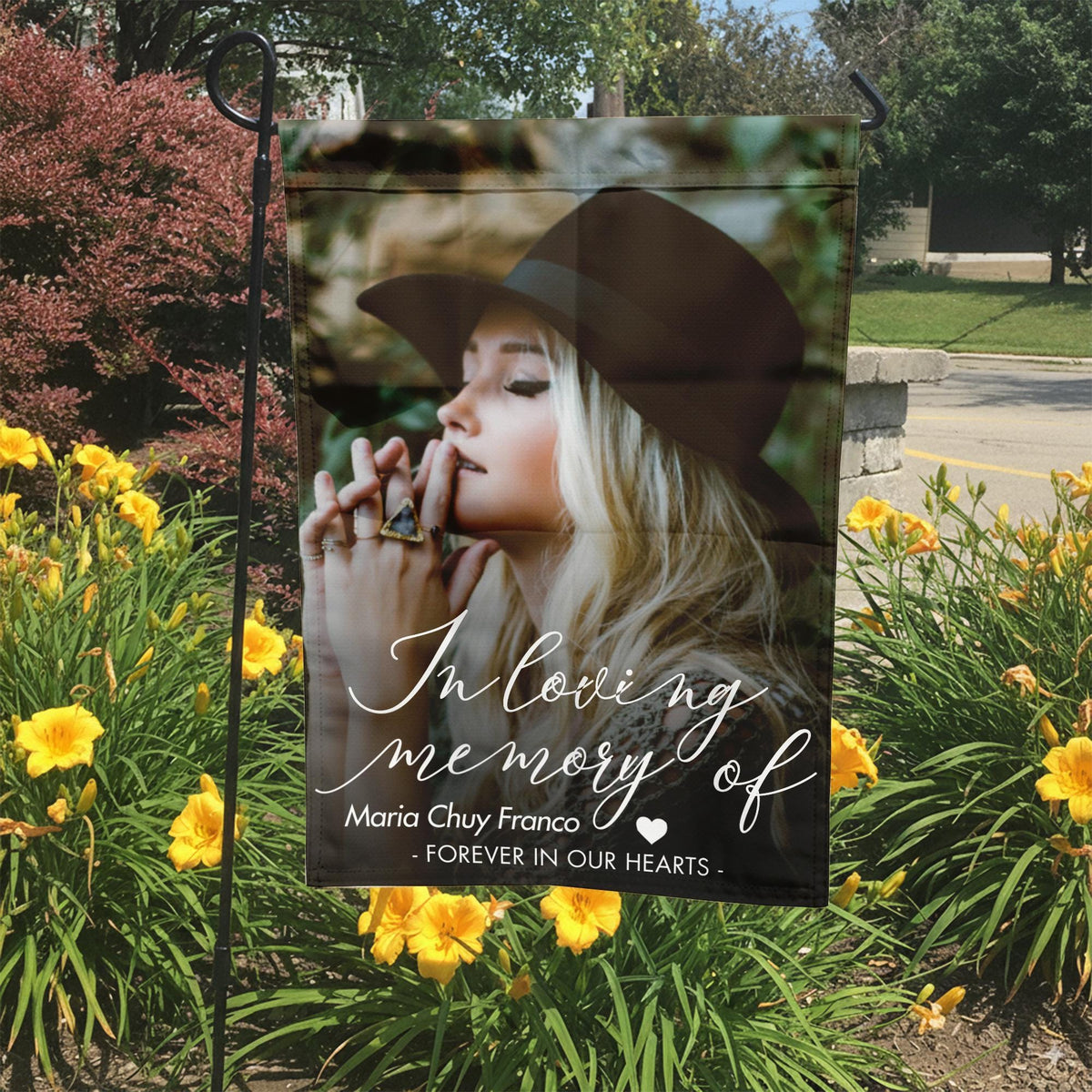 In loving memory photo garden flag with a portrait and name in a garden bed with yellow lilies