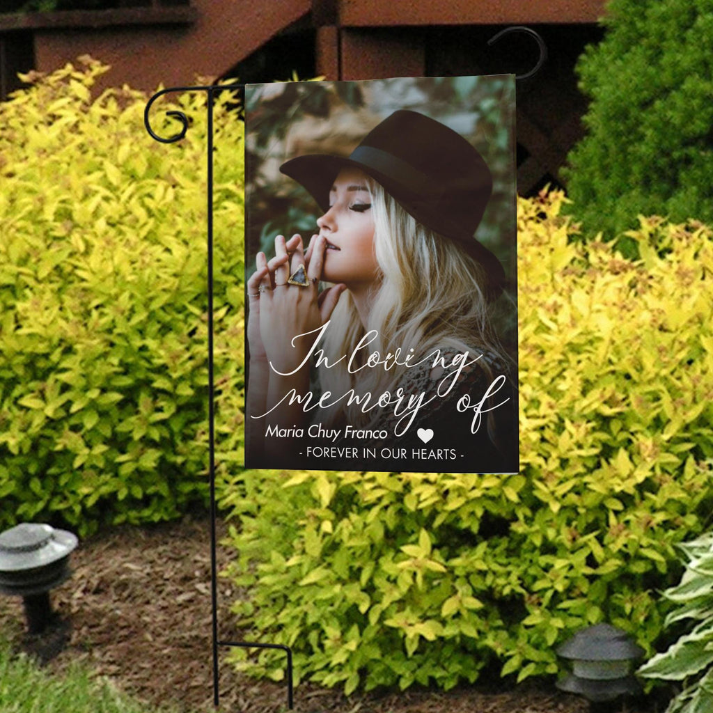 In loving memory photo garden flag with a portrait and name in front of bright yellow shrubs