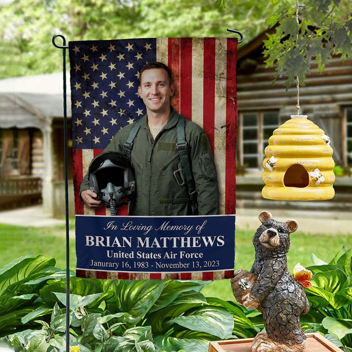 In Loving Memory military photo memorial garden flag on the American flag on a garden stand by a log cabin with a beehive and bear statue