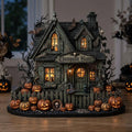 Moss-green haunted house with bats, cobwebs and a Thompson Home sign on a wooden table in front of a dim window