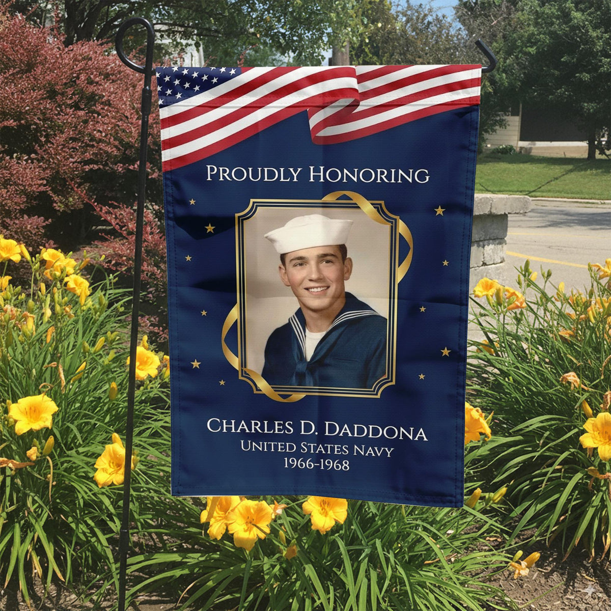 Proudly Honoring military veteran photo memorial garden flag with American flag banner in a garden bed with yellow lilies