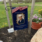 Proudly Honoring military veteran photo memorial garden flag with American flag banner on a garden flag stand in a yard with potted flowers