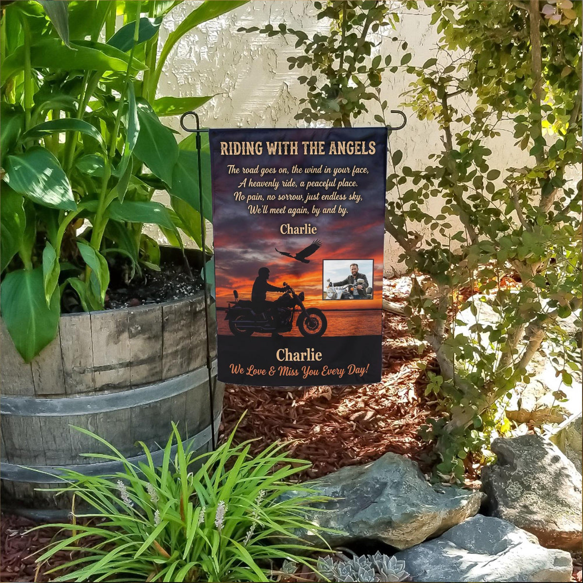 Riding With The Angels motorcycle sunset photo memorial garden flag in a flower bed beside a wooden barrel planter