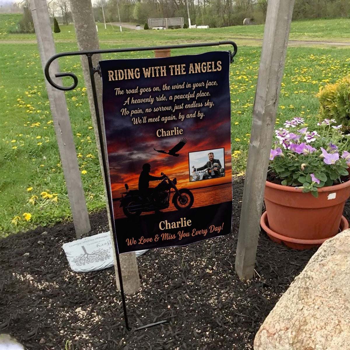 Riding With The Angels motorcycle sunset photo memorial garden flag on a garden flag stand in a yard with potted flowers