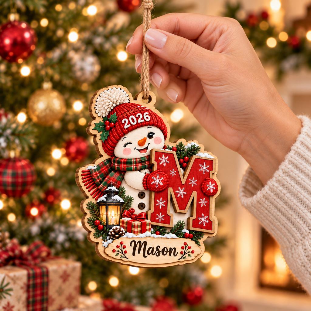 Hand hanging a personalized snowman initial ornament with name and 2026 on tree