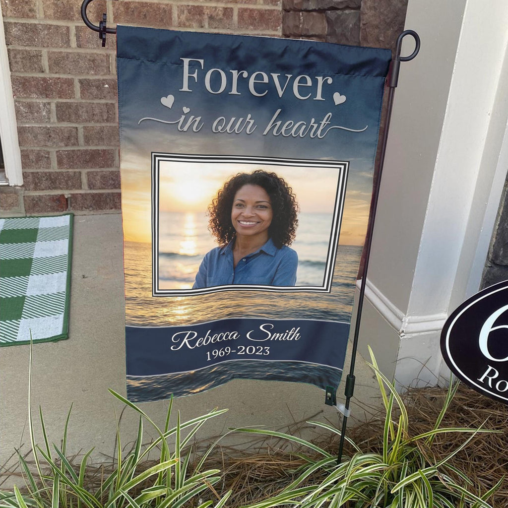 Forever In Our Heart sunset beach photo memorial garden flag with name and years on a stand by a brick front porch