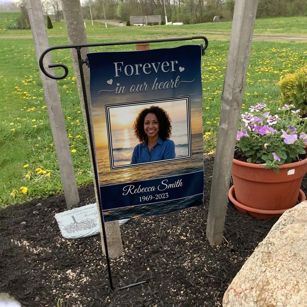 Forever In Our Heart sunset beach photo memorial garden flag with name and years on a garden flag stand in a yard with potted flowers