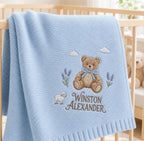 Blue knit blanket folded over a crib rail showing a teddy bear, lamb, lavender and name embroidery up close