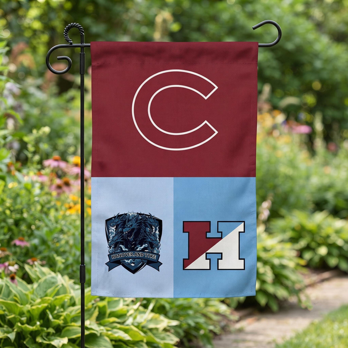 Three-team garden flag with letter logos on a stand in a flower bed