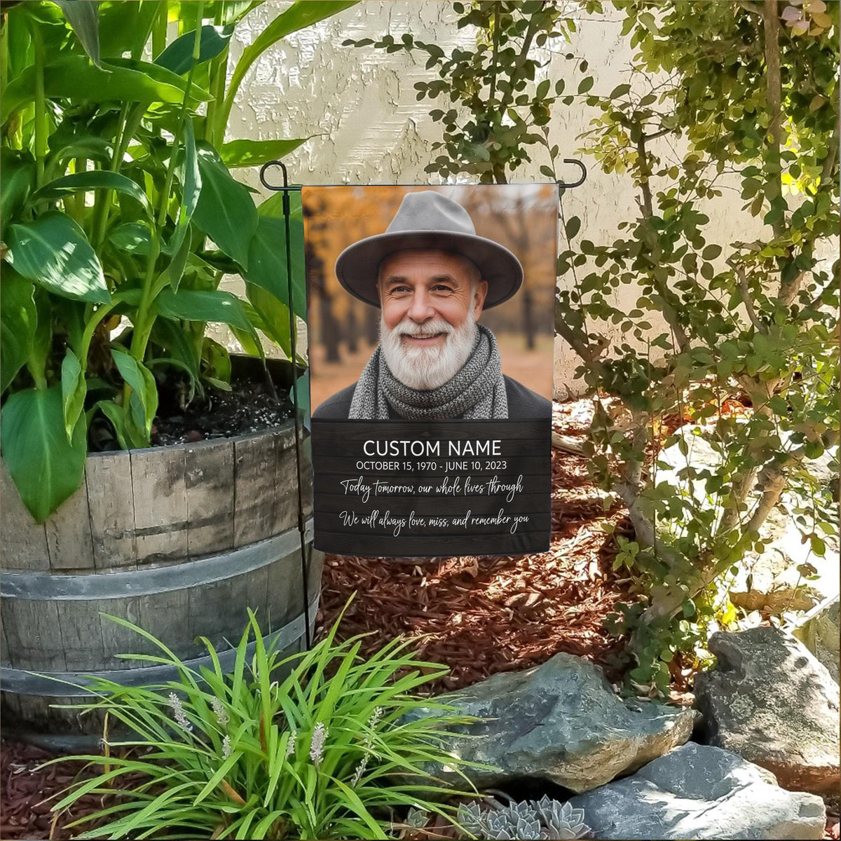 Today Tomorrow Always portrait memorial garden flag with name and dates in a flower bed beside a wooden barrel planter