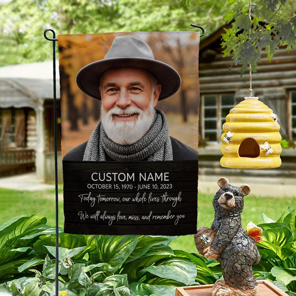 Today Tomorrow Always portrait memorial garden flag with name and dates on a garden stand by a log cabin with a beehive and bear statue