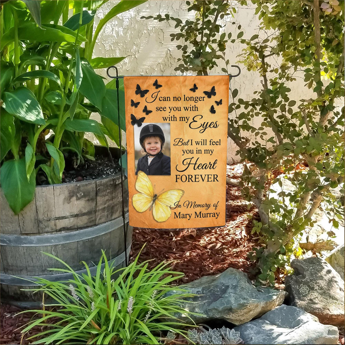 Yellow butterfly I Will Feel You In My Heart photo memorial garden flag in a flower bed beside a wooden barrel planter