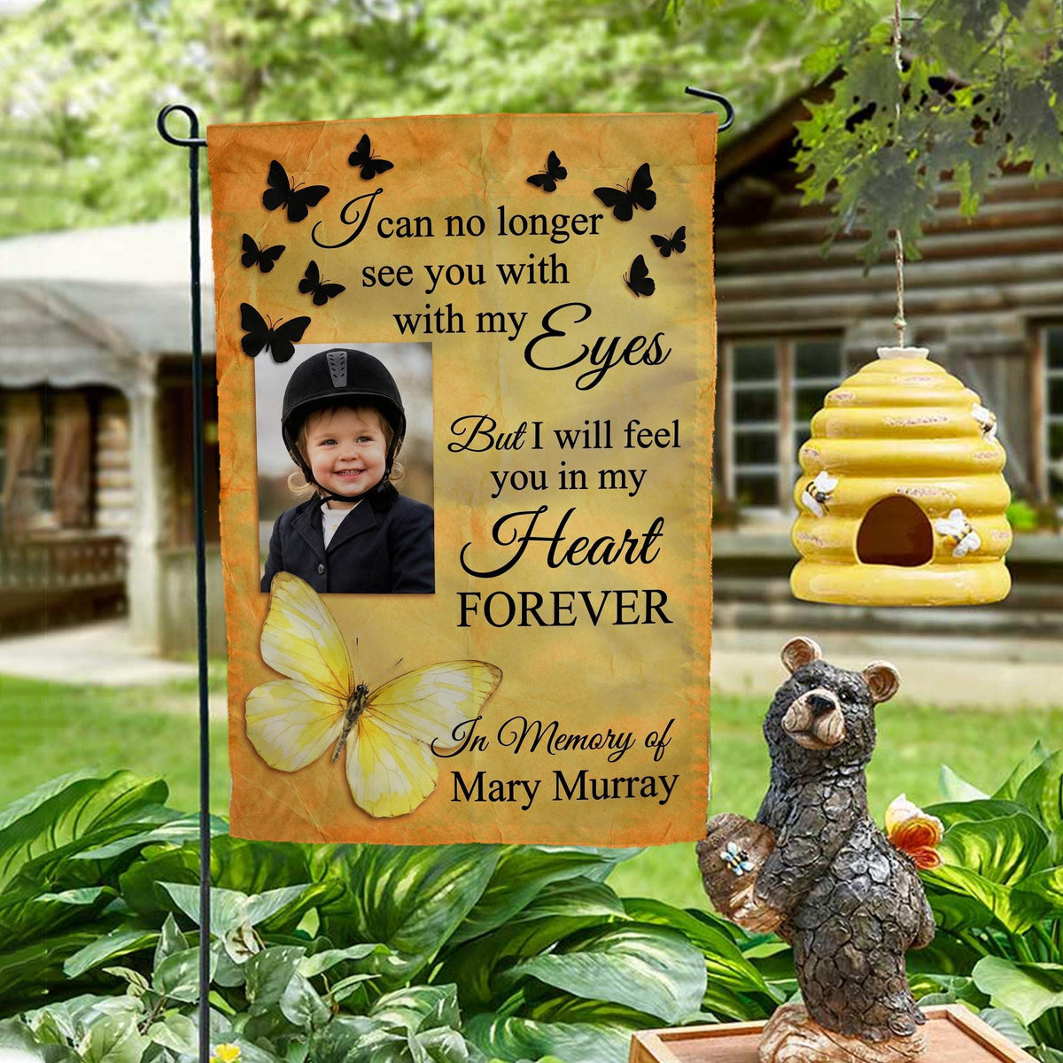 Yellow butterfly I Will Feel You In My Heart photo memorial garden flag on a garden stand by a log cabin with a beehive and bear statue